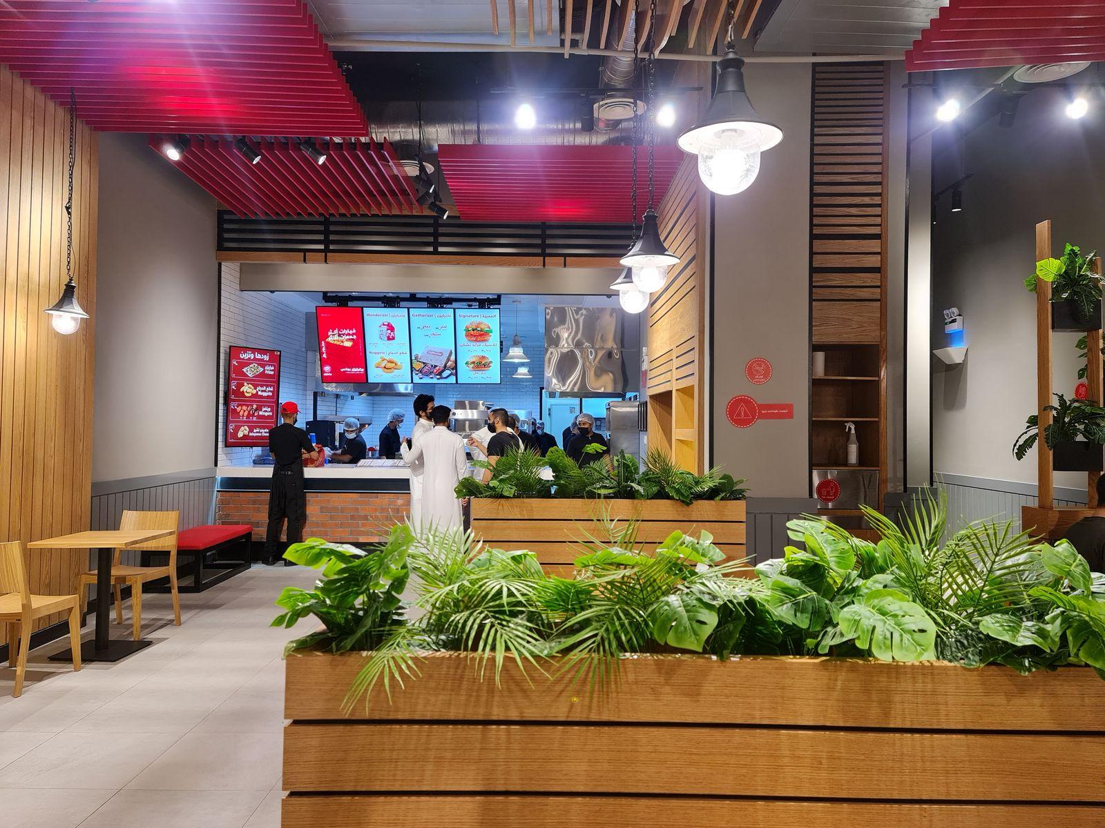 Burgerizzr, Makkah: timber planter boxes dividing the dining hall under a red slatted ceiling