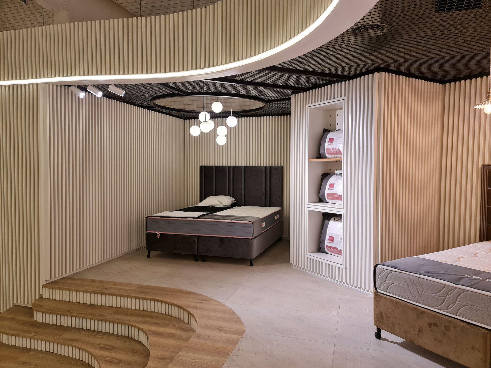 Lyvva showroom, Buraida: a bed on a stepped timber platform under a cluster of globe pendants