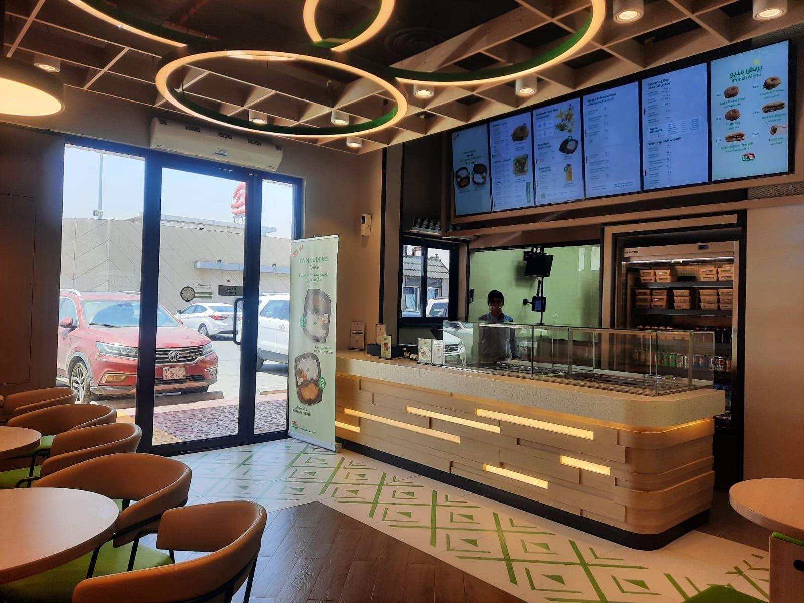 Saldwich, Riyadh: a timber-strip service counter with inset light lines on a patterned tile floor