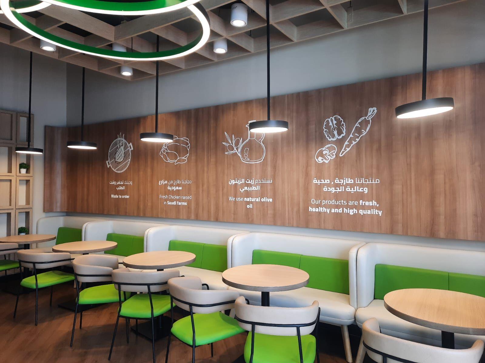 Saldwich, Riyadh: banquette seating along an illustrated timber wall, under ring pendants