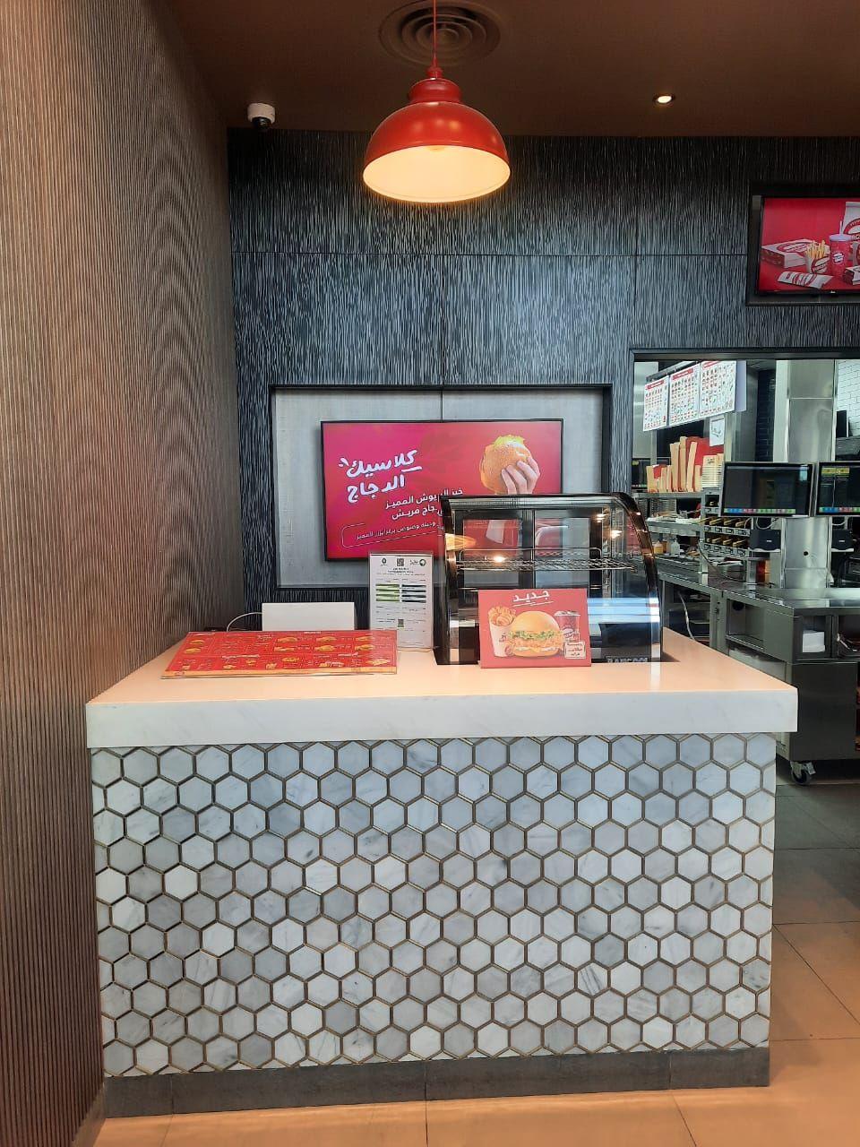 Burgerizzr, Riyadh: an order counter clad in hexagon mosaic under a red pendant, with wood-grain wall panels