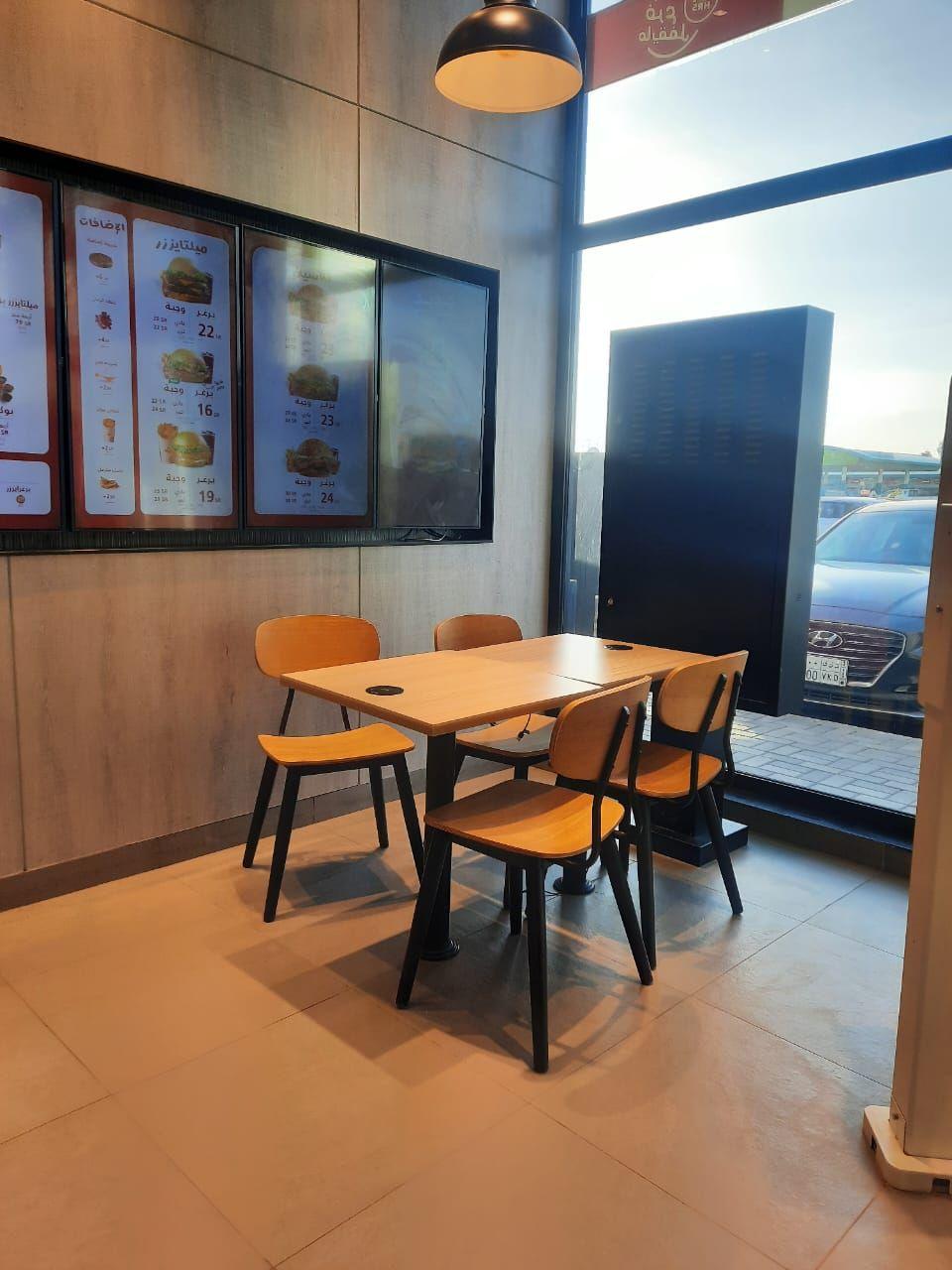Burgerizzr, Riyadh: a dining corner beside full-height glazing and backlit menu boards
