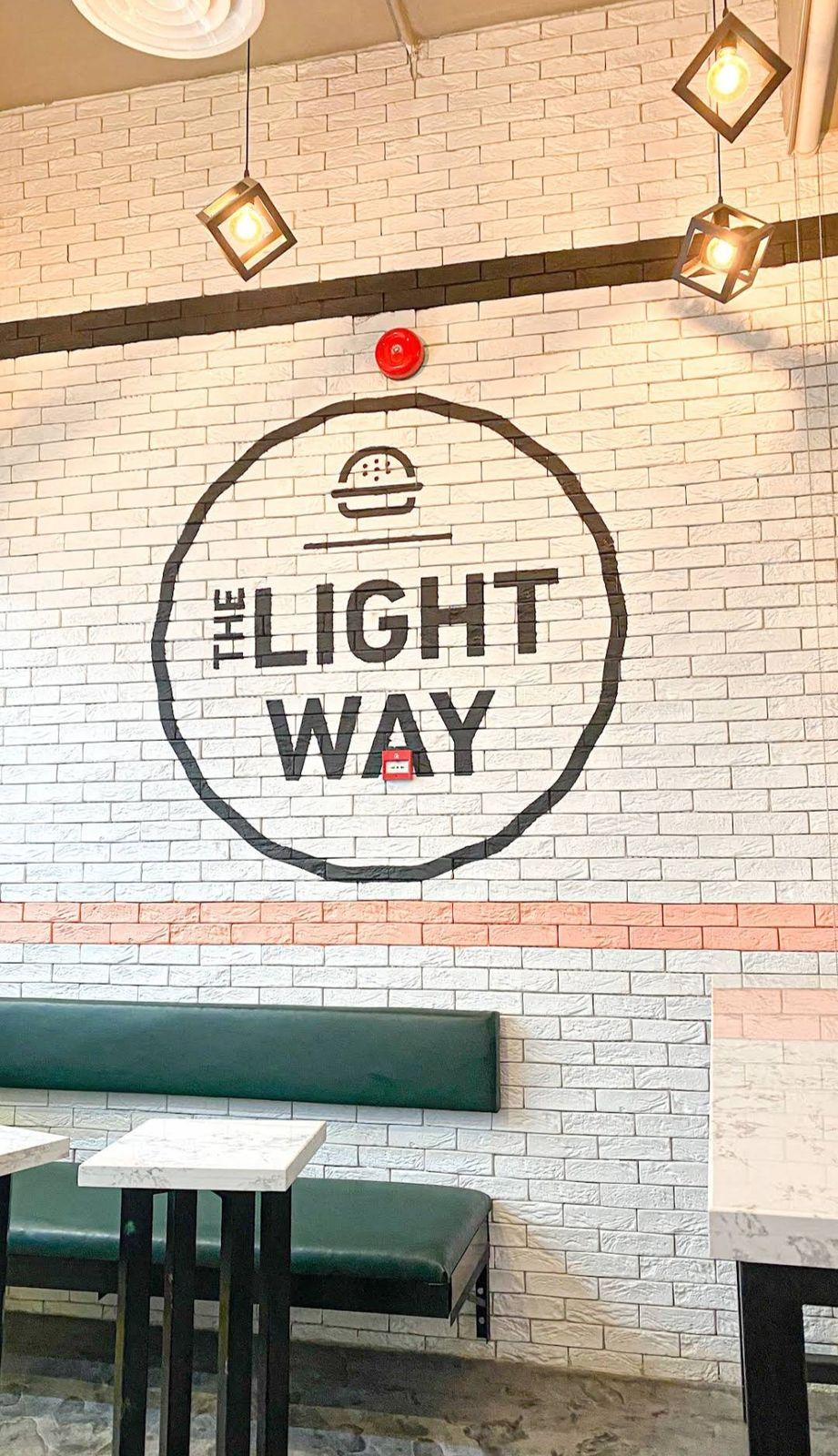 The Light Way Burger, Riyadh: the painted logo on a white brick wall above banquette seating