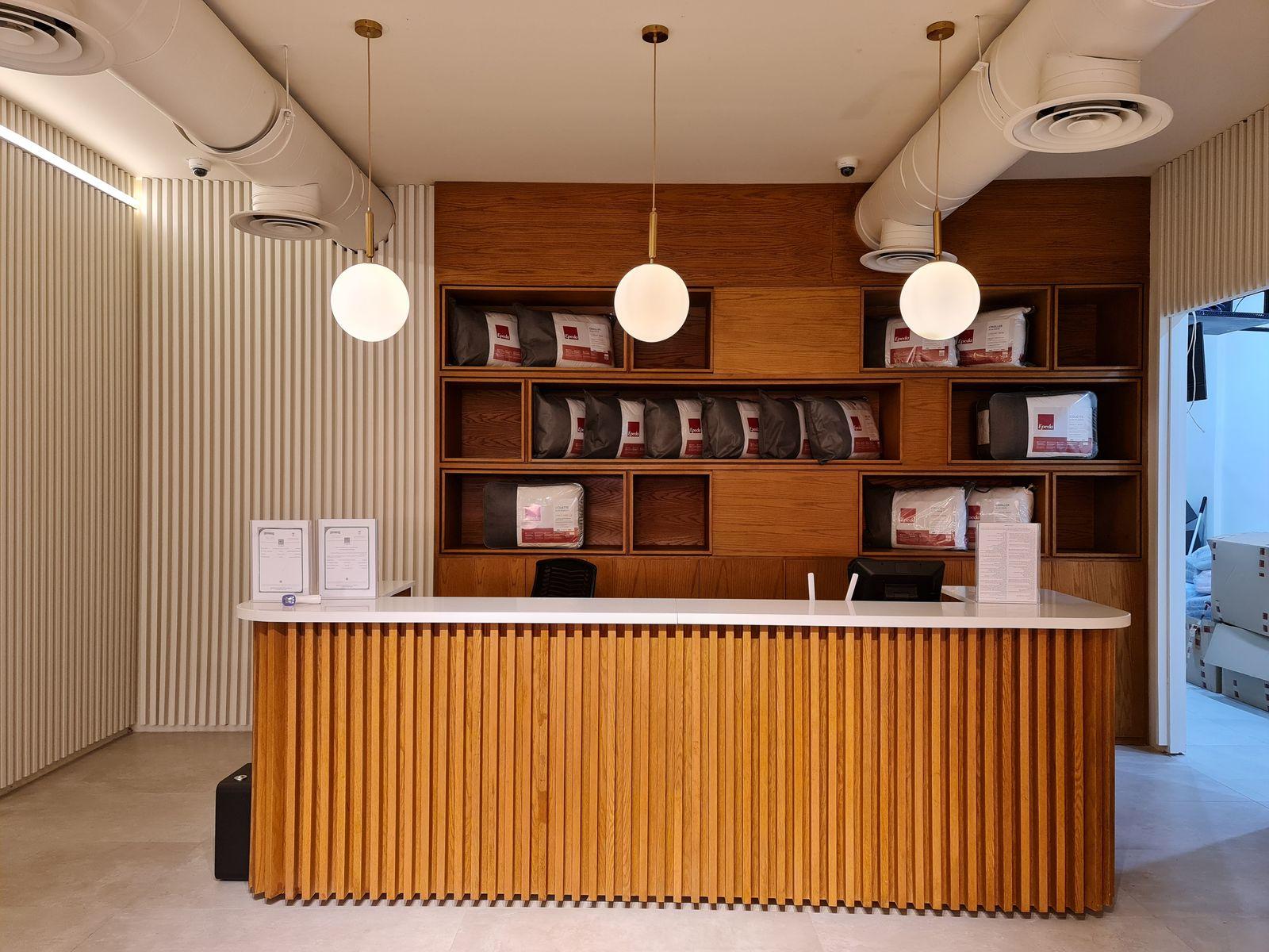 Lyvva showroom, Riyadh: a fluted timber reception desk in front of a shelving wall, under globe pendants